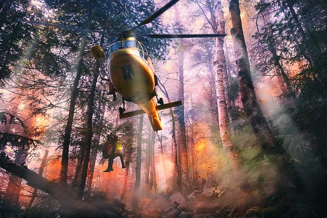 A helicopter flying over trees with smoke coming from it.