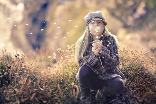 A woman sitting in the grass blowing on a dandelion.