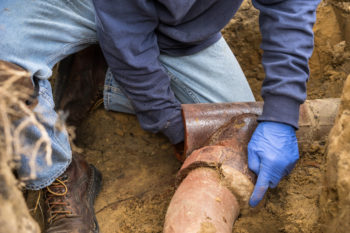 A person in blue gloves is working on a pipe.