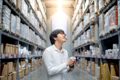 A man holding a pen in his hand while standing next to shelves.