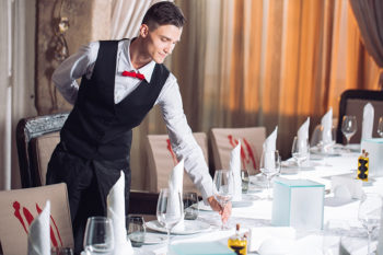 A waiter is setting the table for someone.